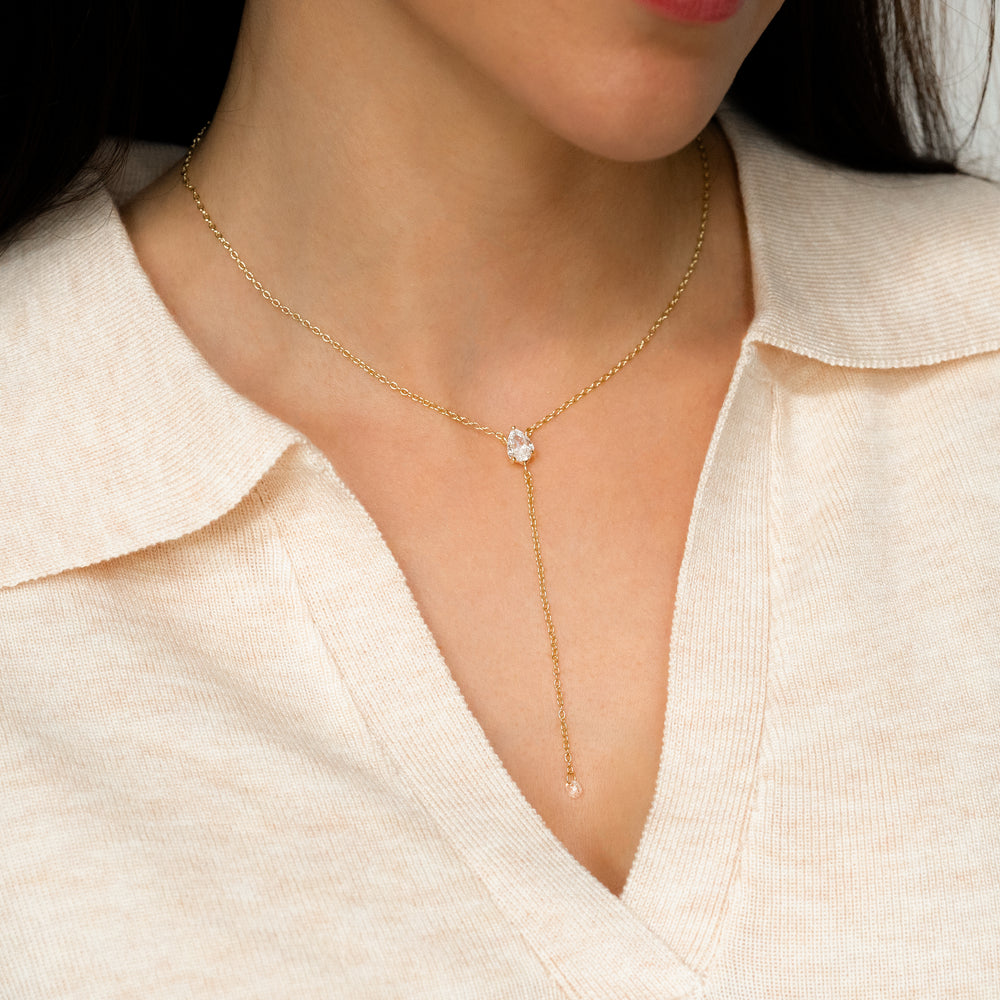 Gold necklace with a two gemstone pendants worn by a person in a light-colored shirt.
