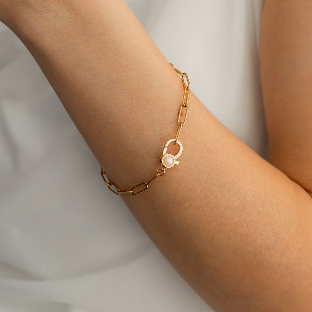 Gold bracelet with a pearl charm on a wrist against a white background