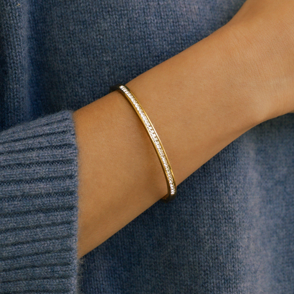 Gold bracelet on a wrist against a blue sweater background