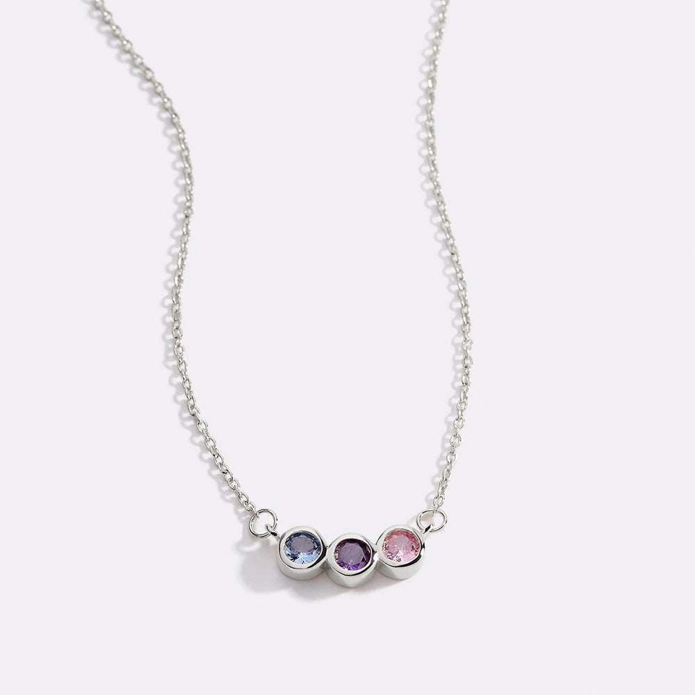 A dainty gold-colored necklace featuring a series of round charms with multicolored birthstones on a black background.