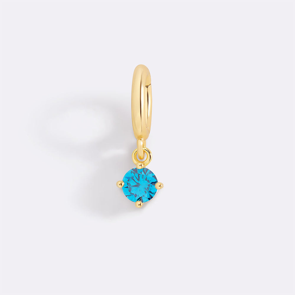 Gold earring with a blue gemstone on a light gray background