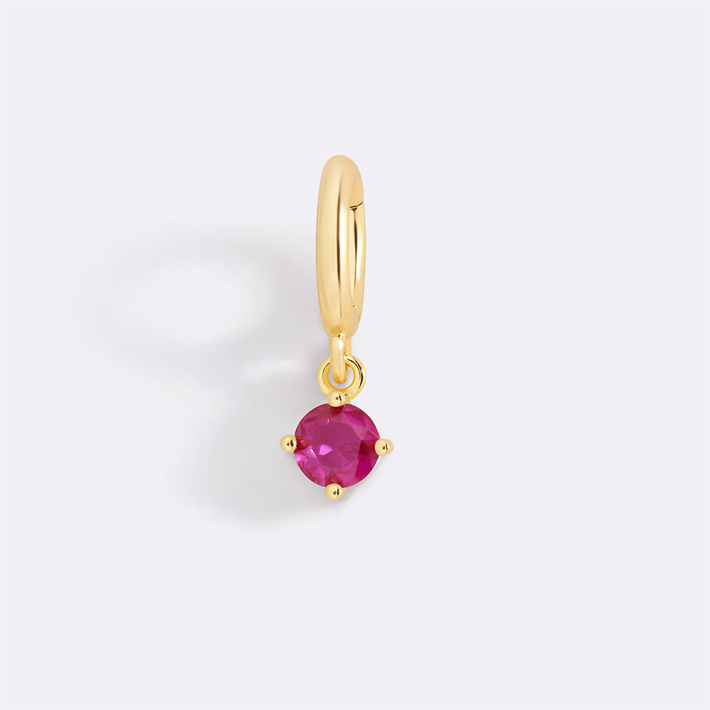 Gold earring with a red gemstone on a light gray background