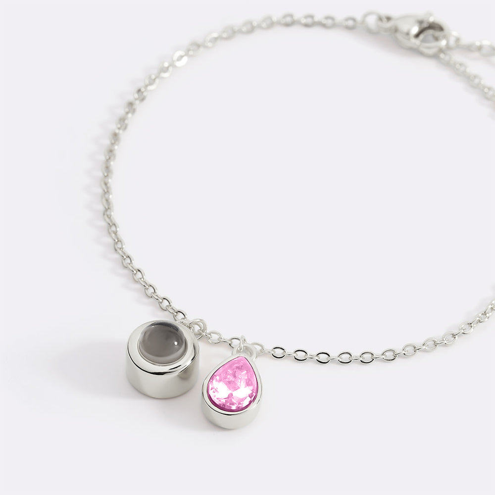 Silver bracelet with a pink teardrop charm and gray round charm on a white background