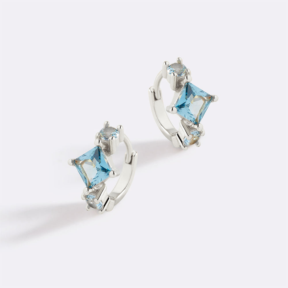 Silver hoop earrings with blue gemstones on a light gray background