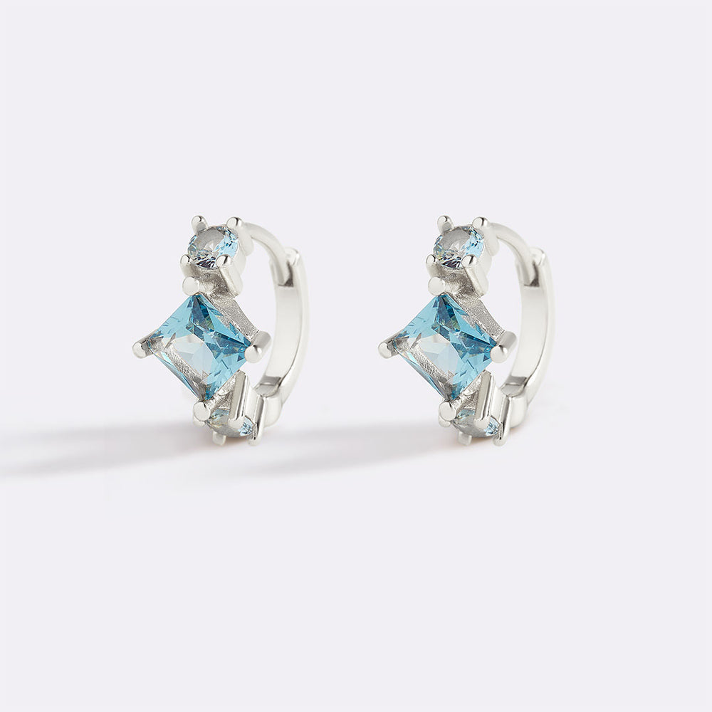 Pair of silver hoop earrings with blue gemstones on a white background
