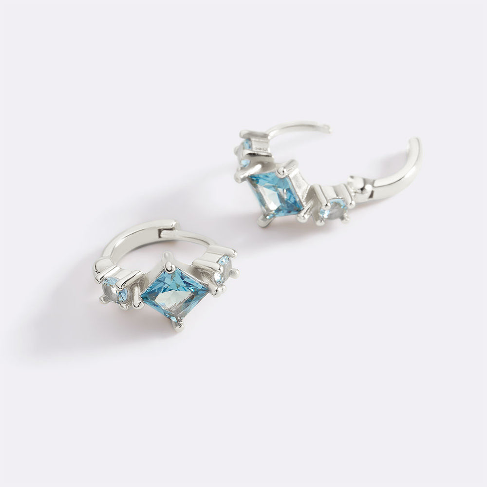 Silver hoop earrings with blue gemstones on a white background