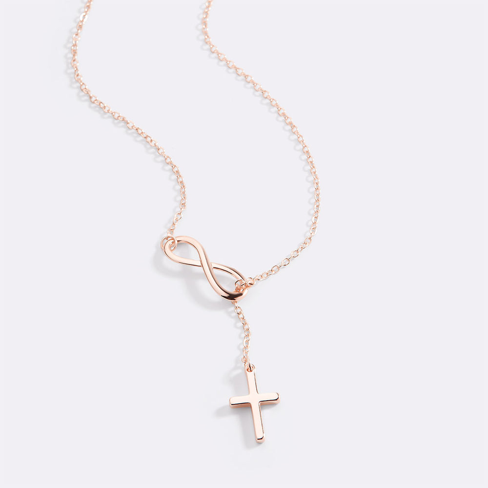 Rose gold necklace with an infinity symbol and cross pendant on a light gray background