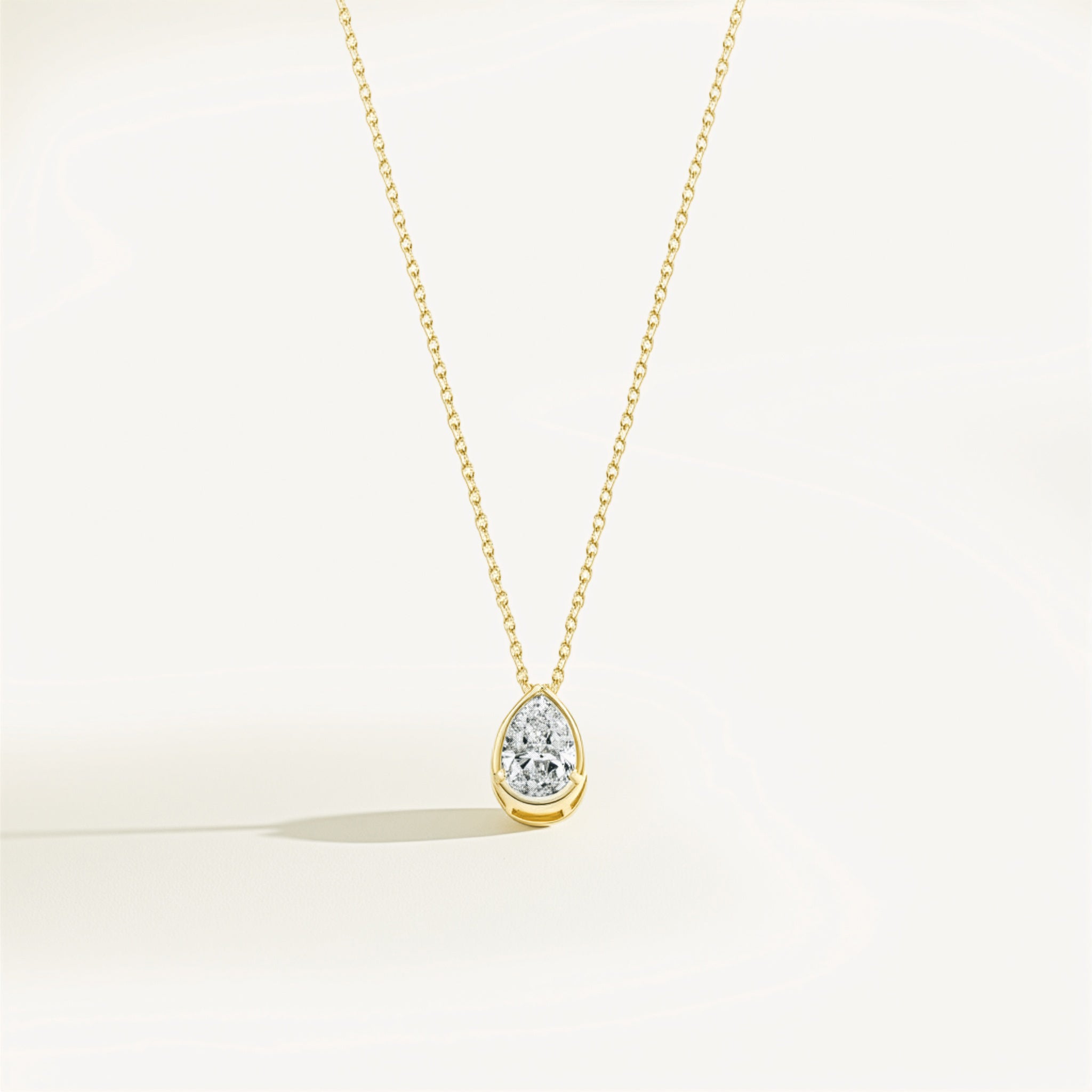 Gold necklace with a teardrop-shaped moissanite pendant on a light beige background
