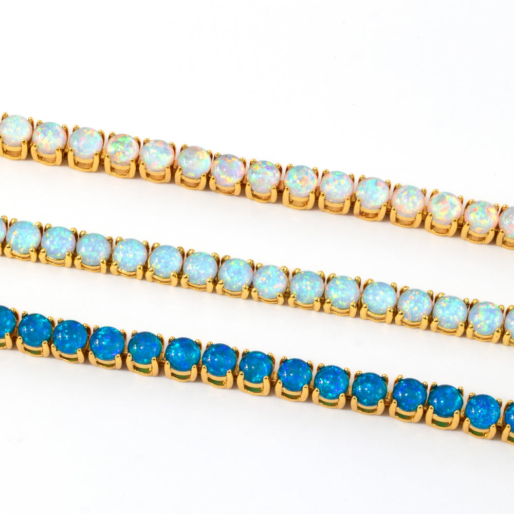Three gold opal tennis bracelets laid side by side on a white background, in white, light blue, and dark blue opal.