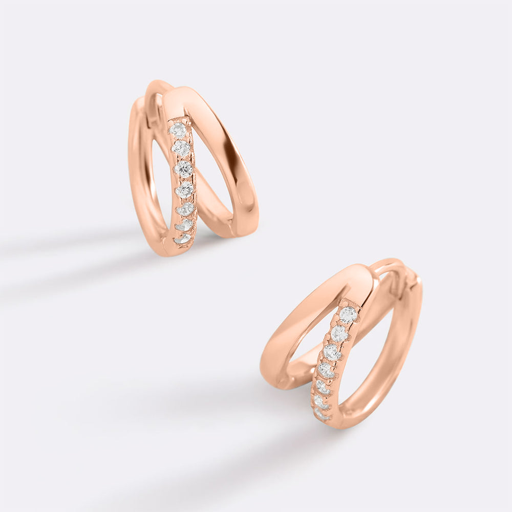 Rose gold hoop earrings with embedded diamonds on a light gray background