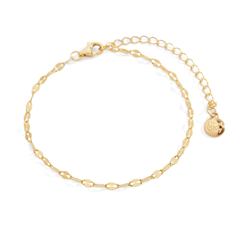 Gold bracelet with a small round charm on a light gray background