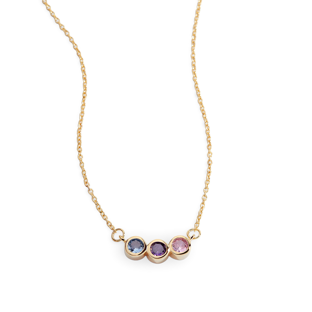 A dainty gold-colored necklace featuring a series of round charms with multicolored birthstones on a black background.
