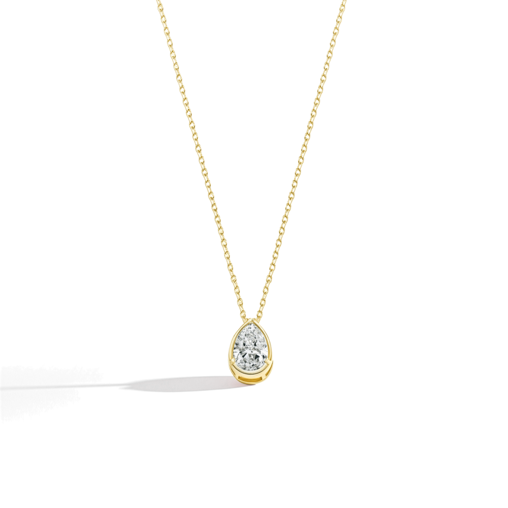 Gold necklace with a teardrop-shaped diamond pendant on a light beige background