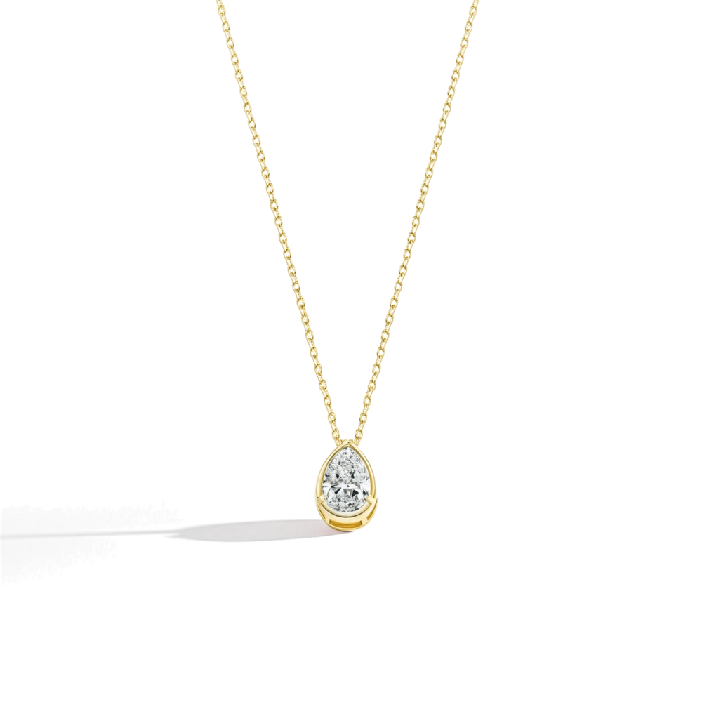 Gold necklace with a teardrop-shaped moissanite pendant on a light beige background