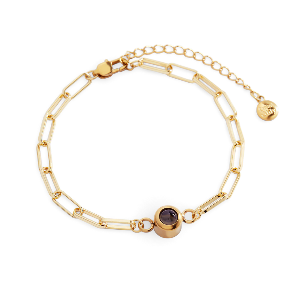 Gold chain bracelet with a purple gemstone on a white background