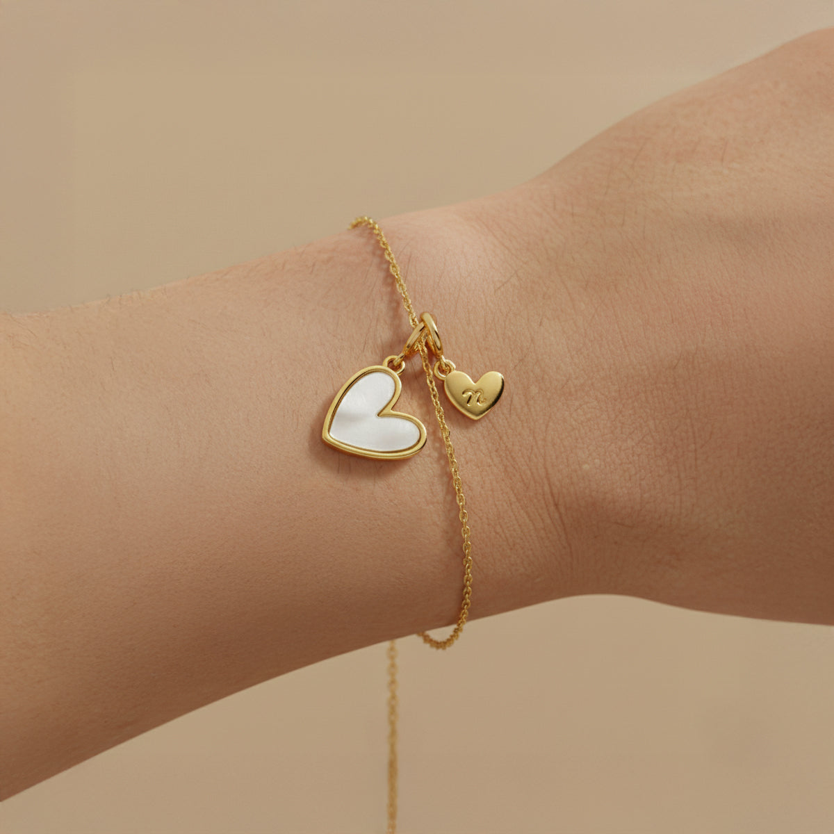 Gold bracelet with heart-shaped charms on a wrist against a beige background