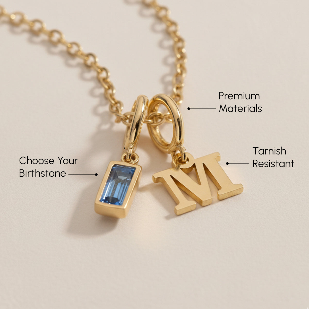 Gold necklace with birthstone and letter 'M' charm on a beige background