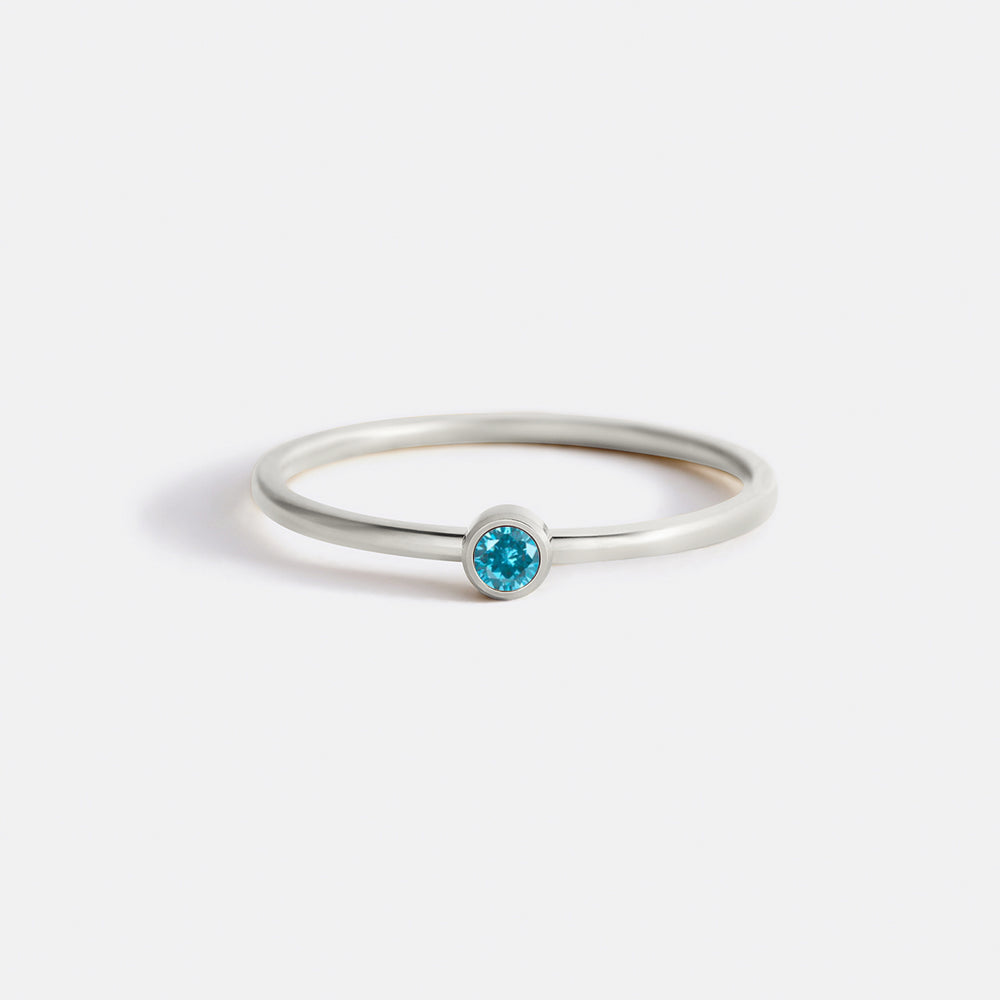 A gold-colored minimalist stacking band with a bezel-set blue birthstone.