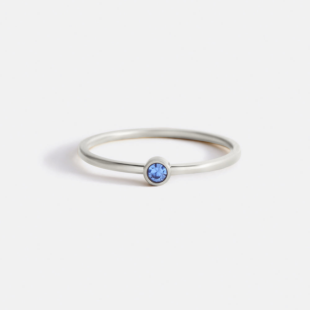 A gold-colored minimalist stacking band with a bezel-set blue stone.