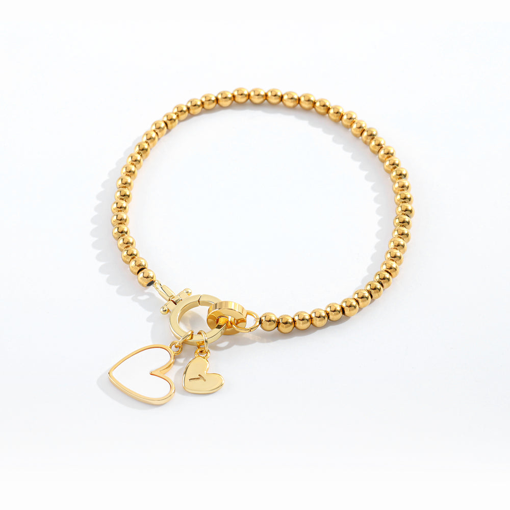 Gold beaded bracelet with heart charm on a white background