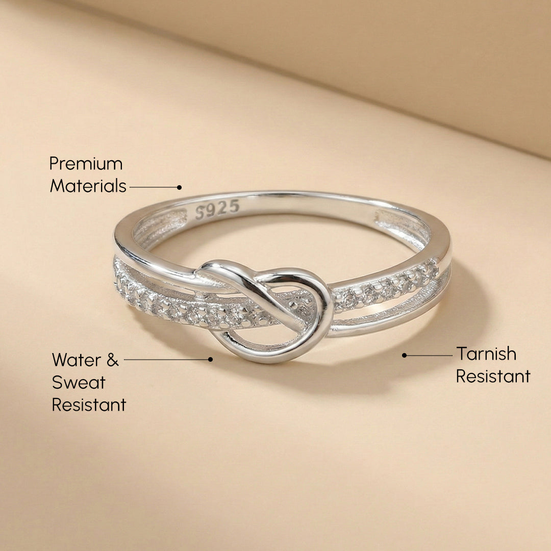 Silver ring with knot design on a beige background, labeled for material, water & sweat resistance, and tarnish resistance.
