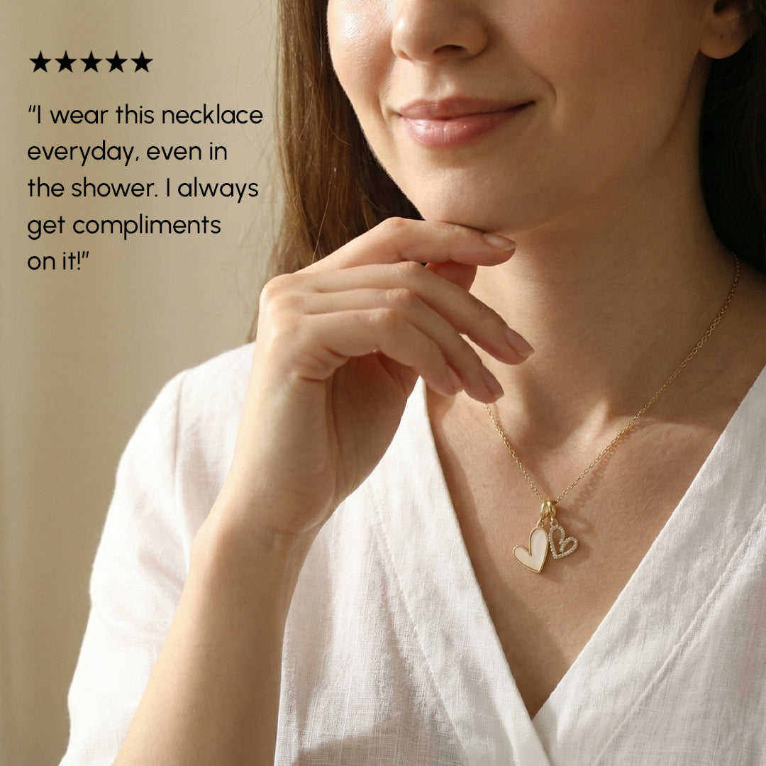 Woman wearing a gold necklace with heart pendants, smiling softly.