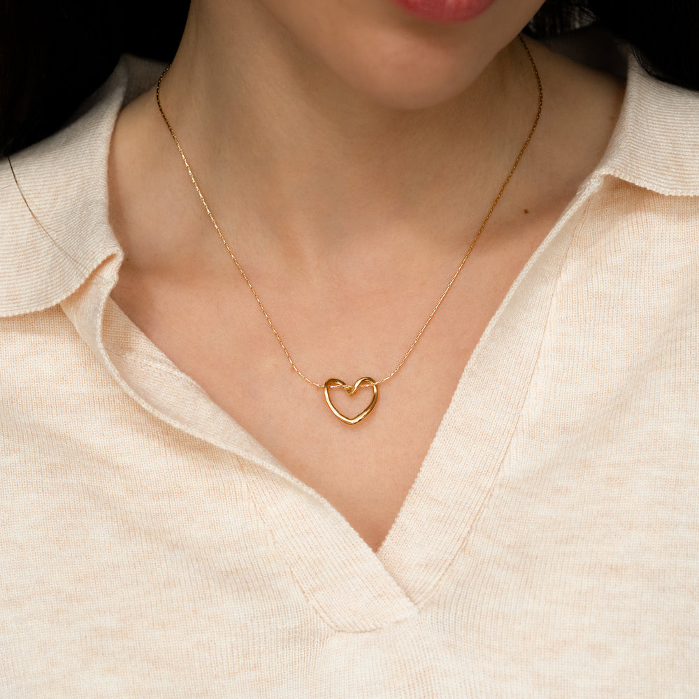 Gold heart-shaped necklace worn by a person in a light-colored shirt.