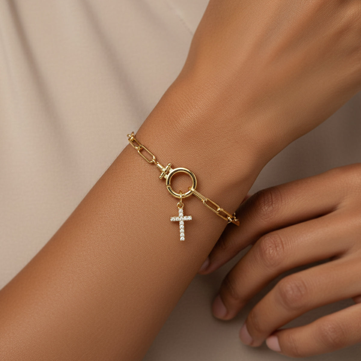 Gold bracelet with a cross charm on a wrist against a neutral background