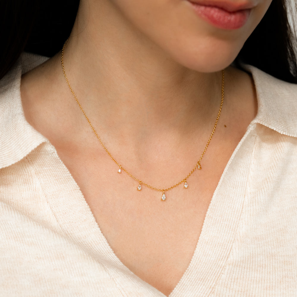 Gold necklace with small pear shaped pendants on a person wearing a white blouse.