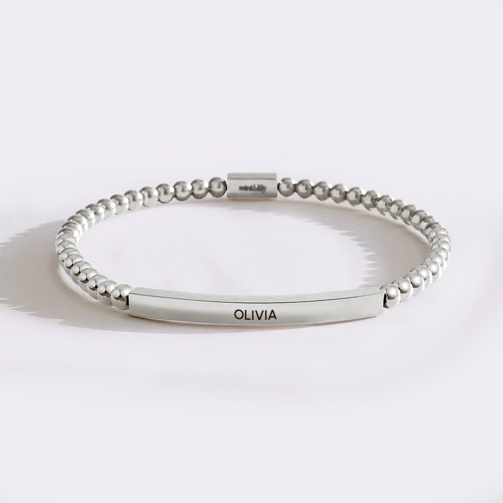 Silver beaded bracelet with a bar section engraved with 'OLIVIA' on a light background