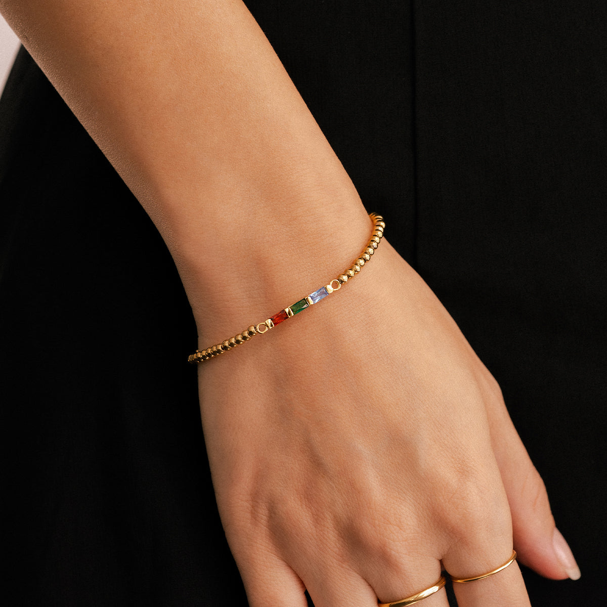 Gold bracelet with colorful beads on a wrist against a black background