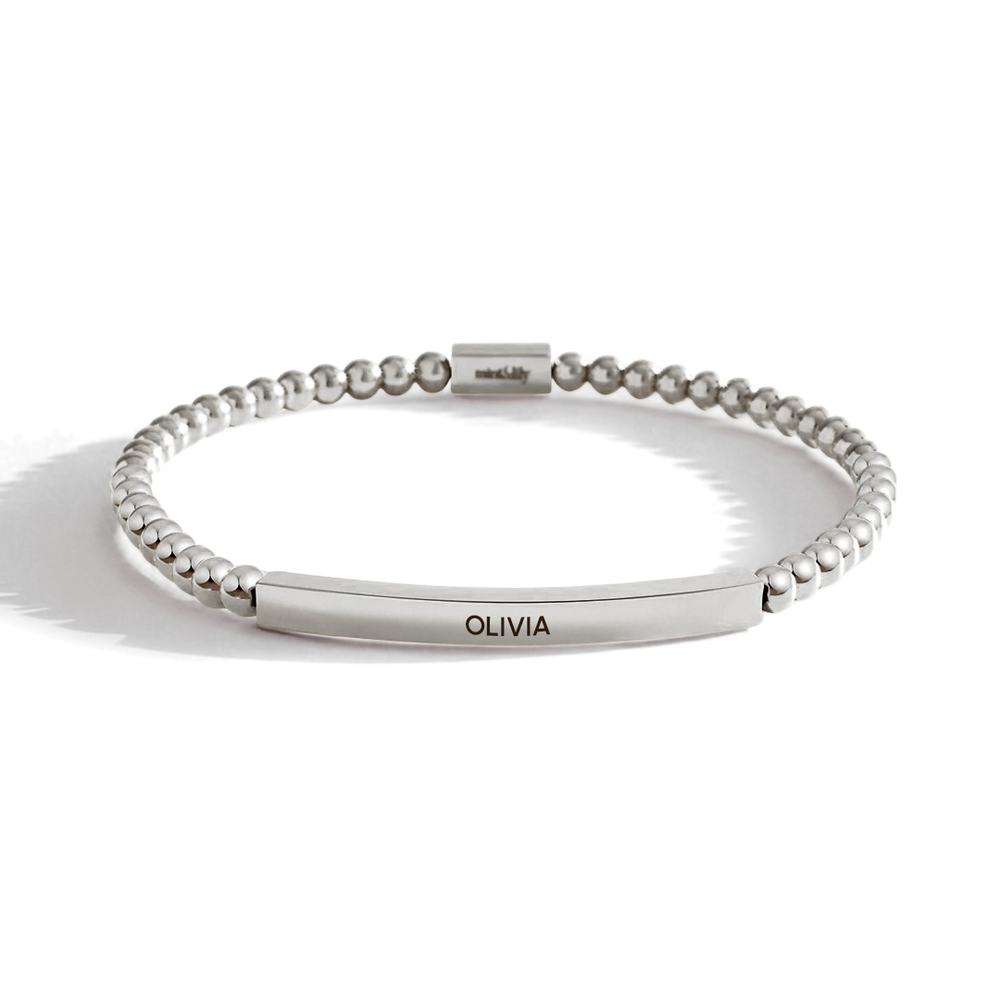 Silver beaded bracelet with a bar section engraved with 'OLIVIA' on a light background