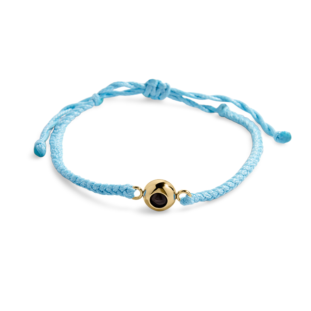 Adjustable blue braided nylon bracelet with a gold-colored circular photo charm in the center, shown with a reflective background.