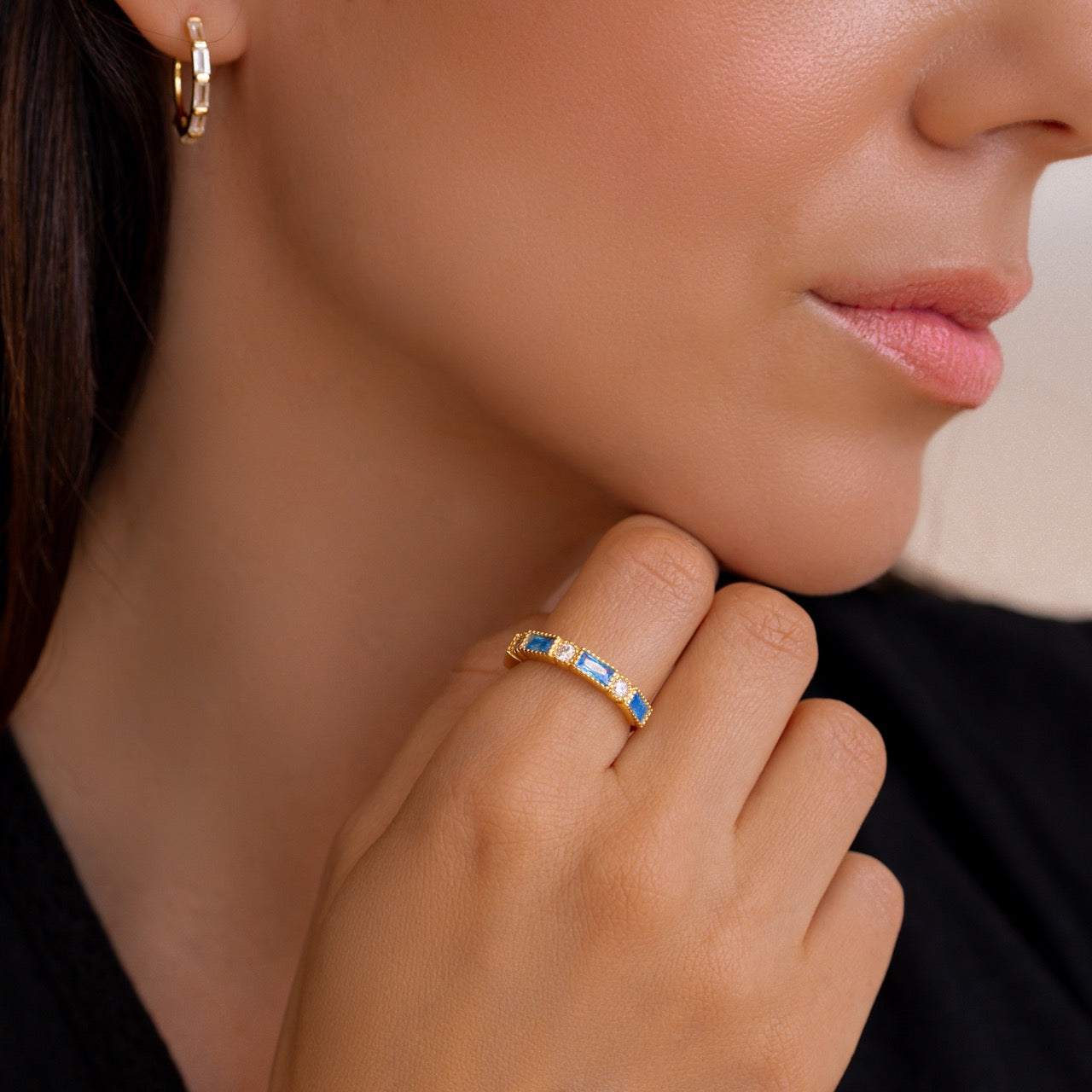 Close-up of a woman's hand wearing a gold ring with gemstones, against a neutral background.