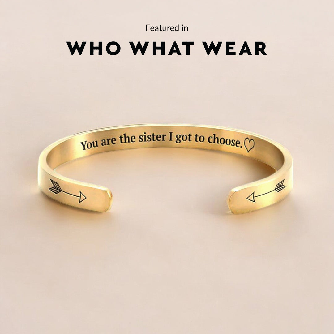 Gold bracelet with engraved message on a beige background, featuring 'WHO WHAT WEAR'.