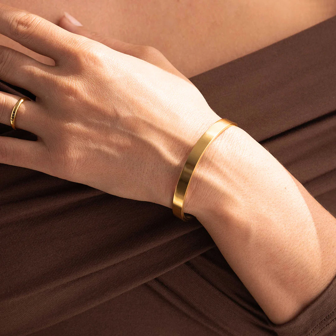 Gold bracelet on a wrist with a neutral background