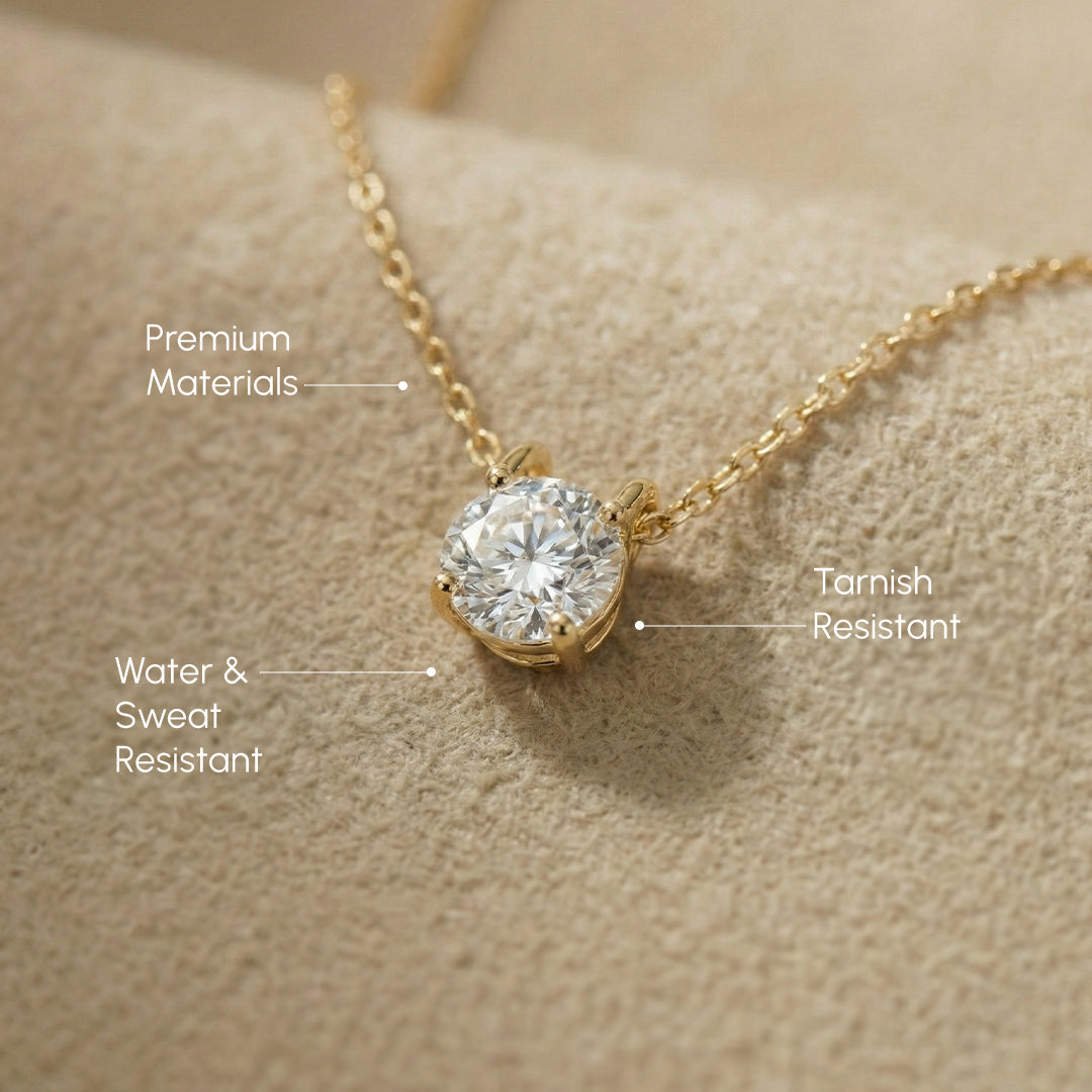 Gold necklace with diamond pendant on a beige surface, labeled for features.