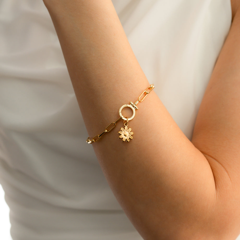 Gold bracelet with a sun charm on a person's wrist against a white background