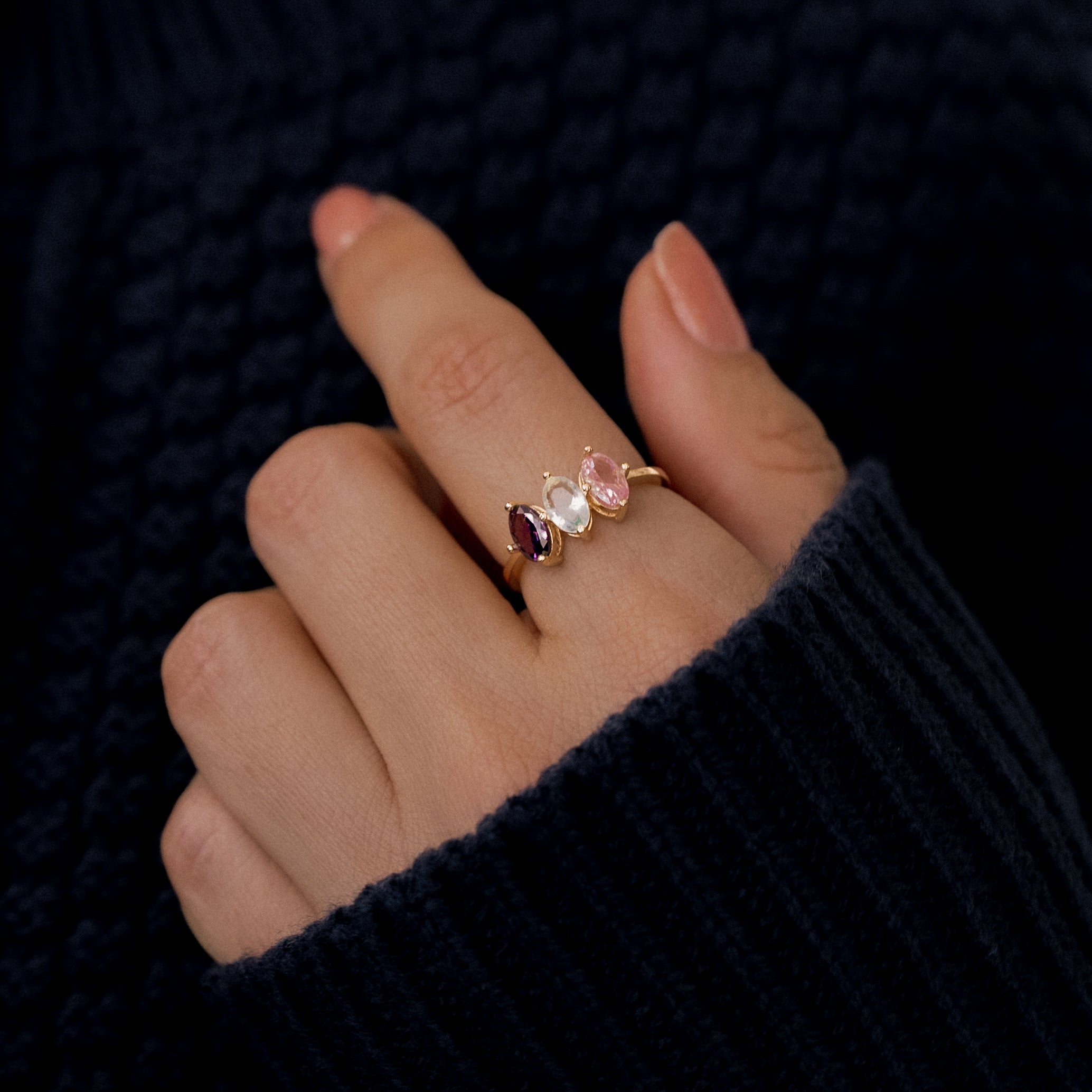 Hand wearing a gold ring with three gemstones against a dark background