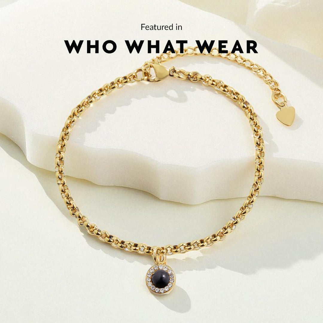 Gold bracelet with a black gemstone on a white fabric background, featuring 'WHO WHAT WEAR'.