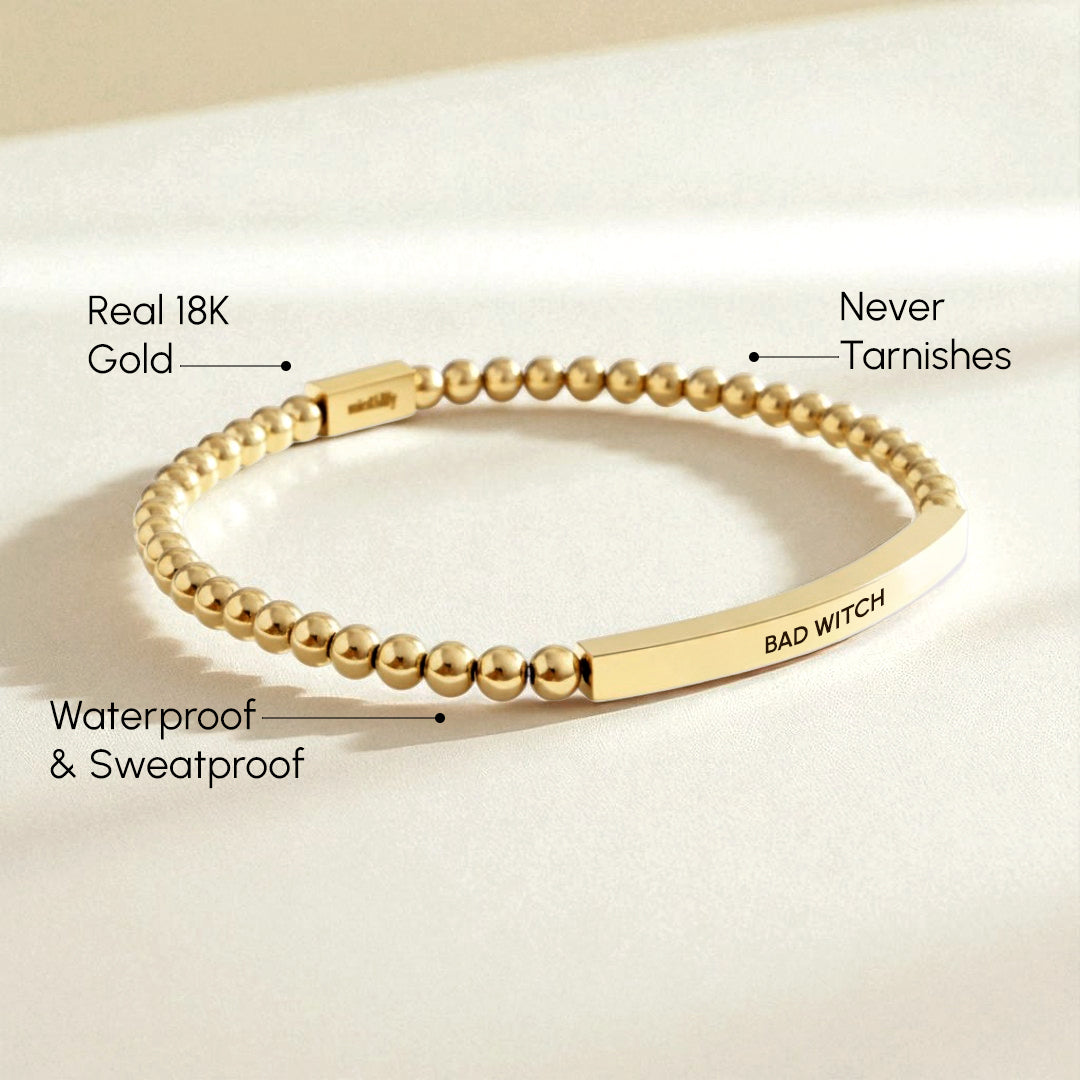 Gold bracelet with 'BAD WITCH' engraving on a beige background