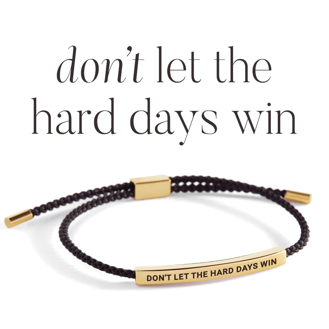 Black braided bracelet with gold clasp and 'DON'T LET THE HARD DAYS WIN' tag on a light gray background.