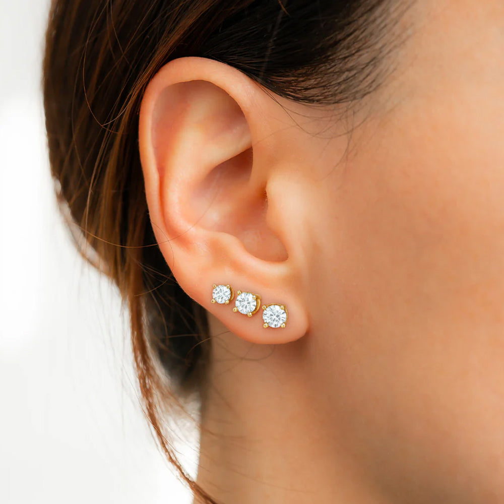 Close-up of an ear wearing three diamond stud earrings on a white background