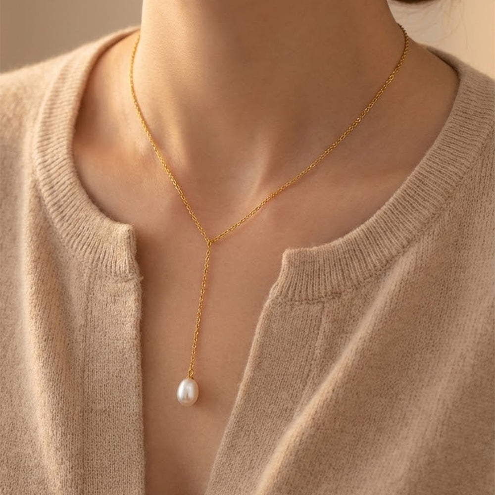 Gold necklace with a pearl pendant worn by a person in a beige sweater.