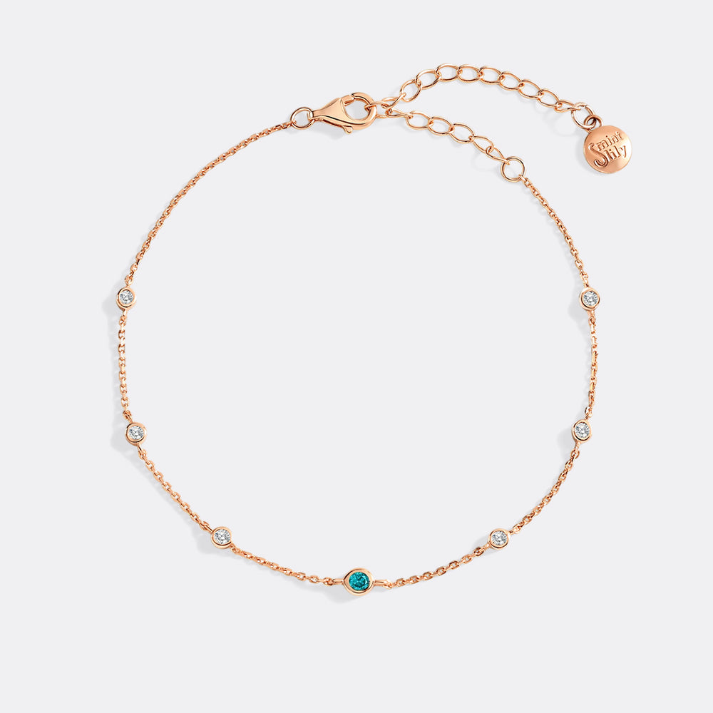 Rose gold bracelet with small gemstones on a light gray background