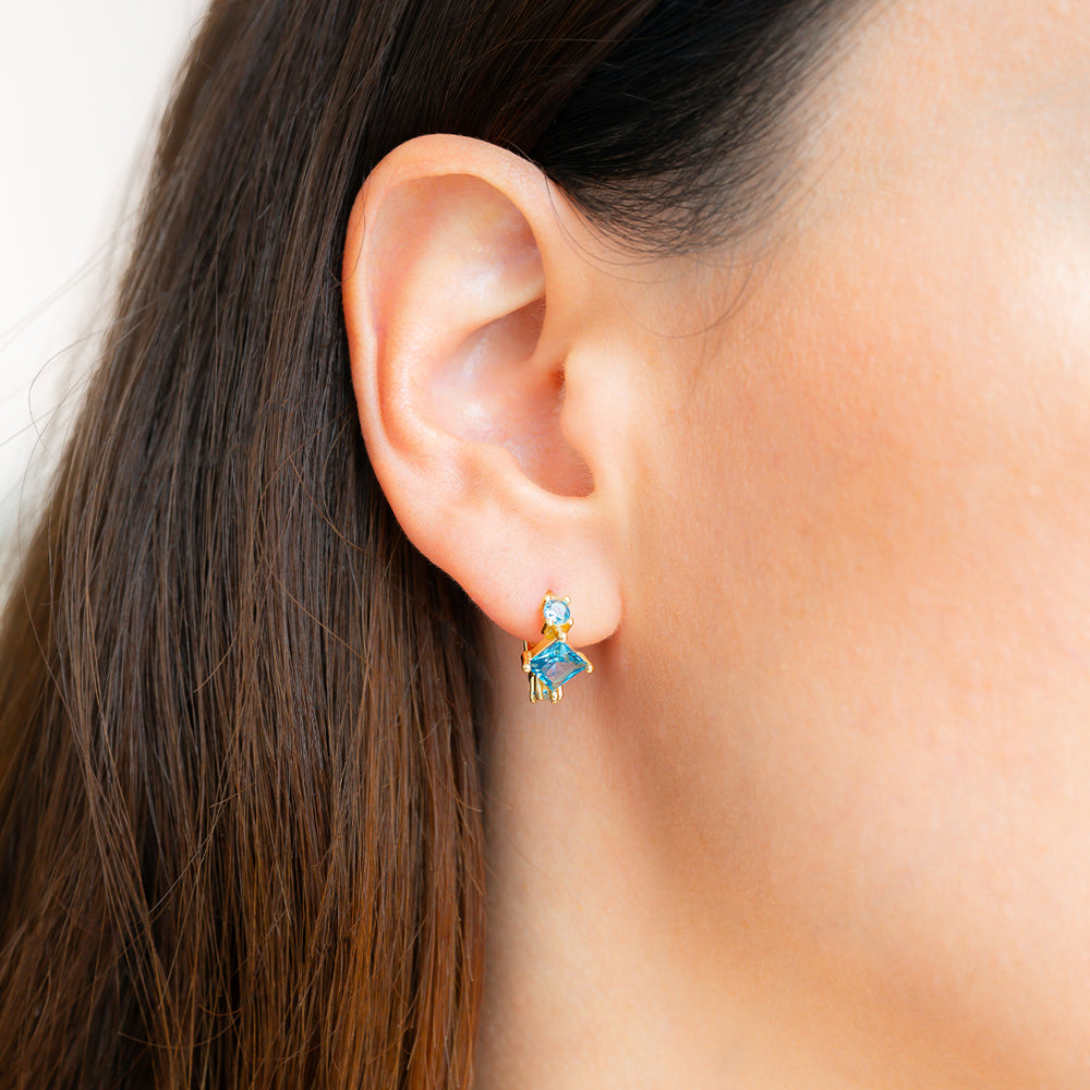Person wearing a blue star-shaped earring with a hand pointing to it.