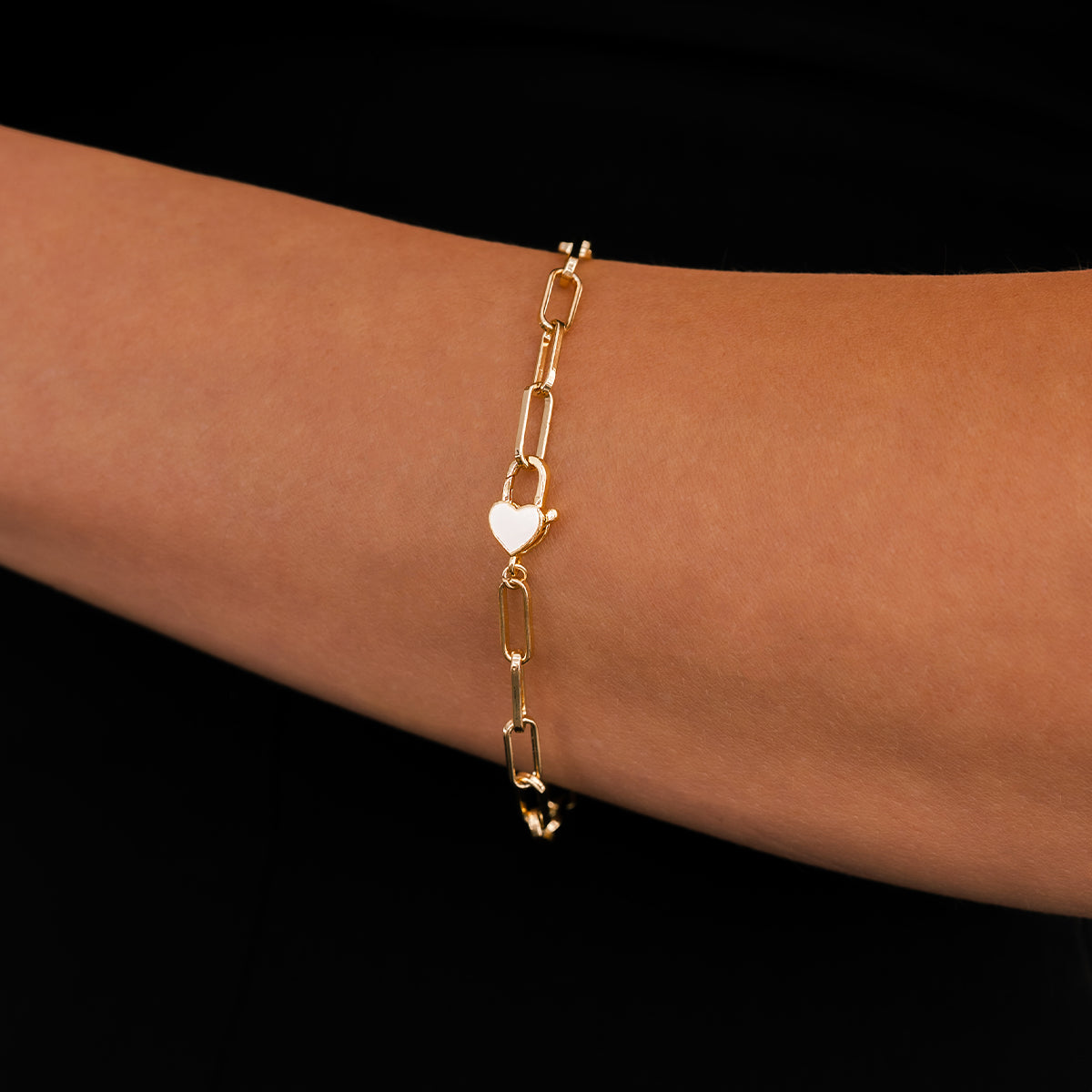 Gold bracelet with heart charm on a wrist against a black background