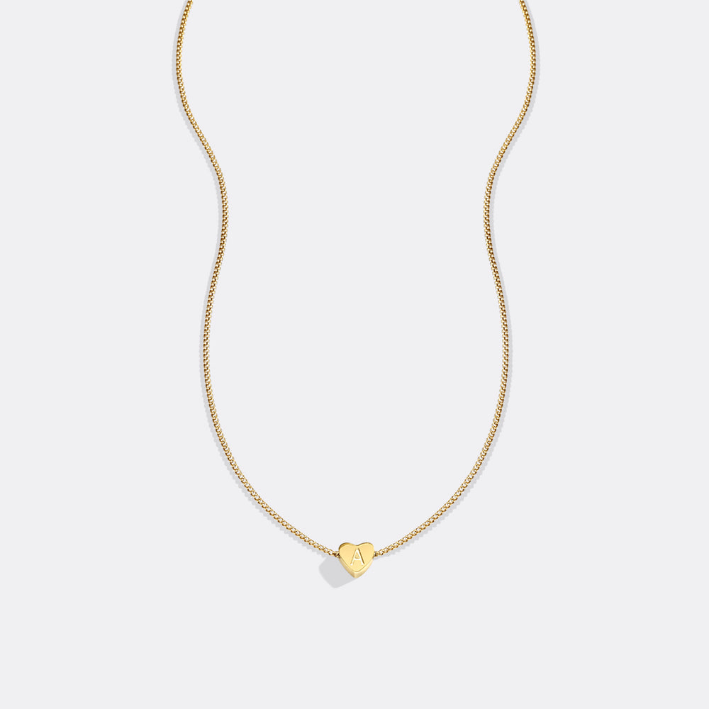 Gold necklace with a heart-shaped pendant on a light gray background