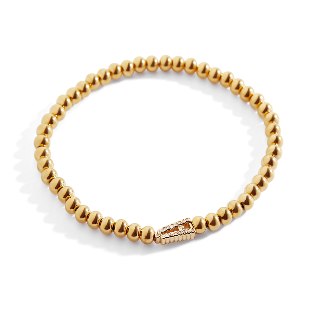 A gold-colored stretch bracelet with a sparkling diamond initial, featuring bead embellishments.