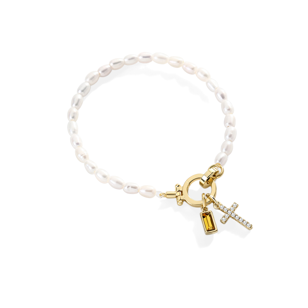 Pearl bracelet with gold charms on a light gray background
